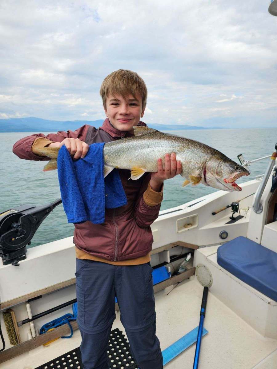 A young boy is holding a large fish on a boat.
