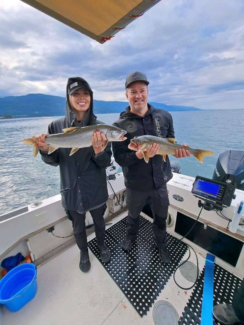 Two men are standing on a boat holding fish.