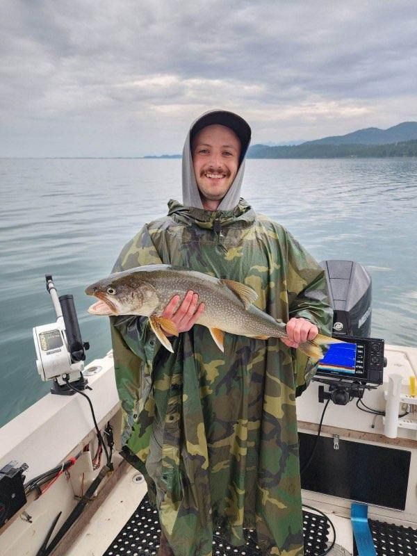 A man in a poncho is holding a large fish on a boat.