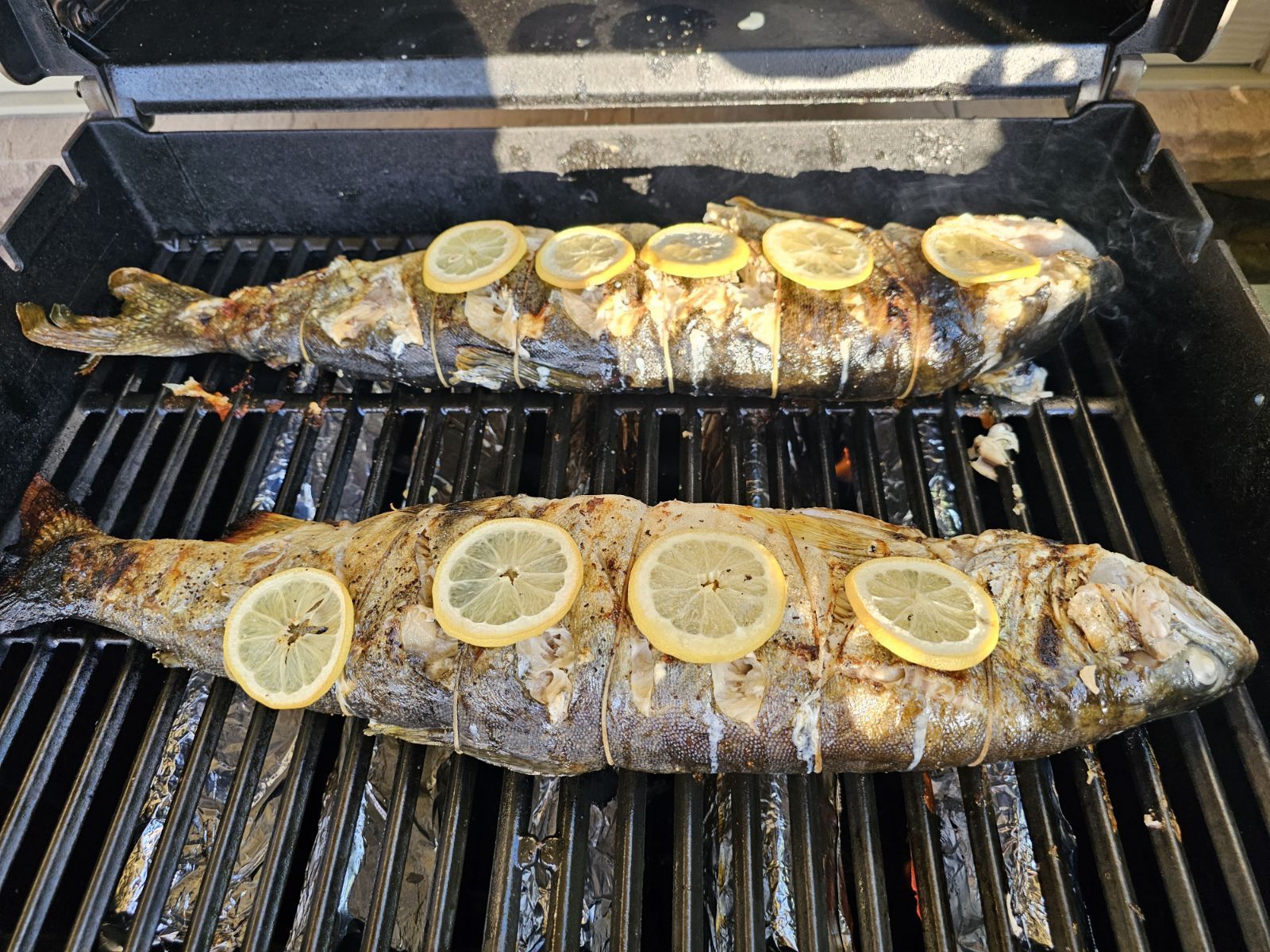 Two fish are cooking on a grill with lemon slices.
