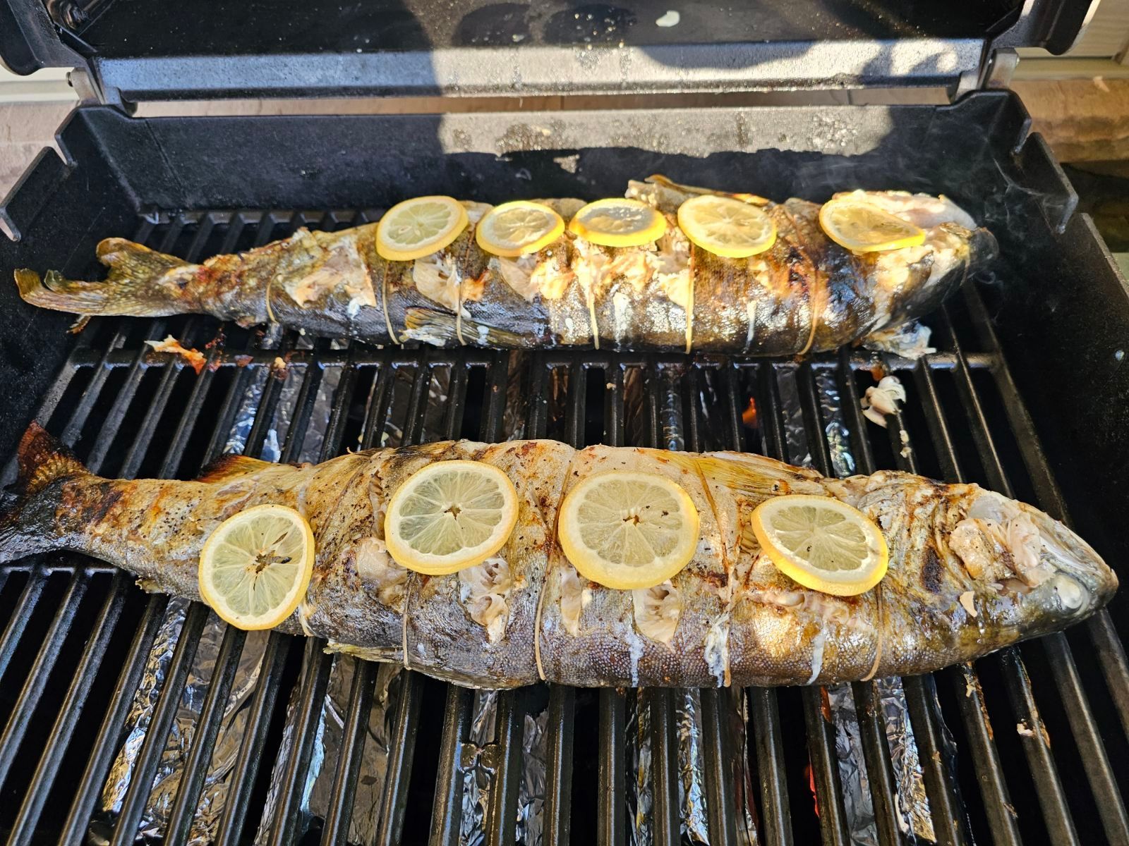 Two fish are cooking on a grill with lemon slices.