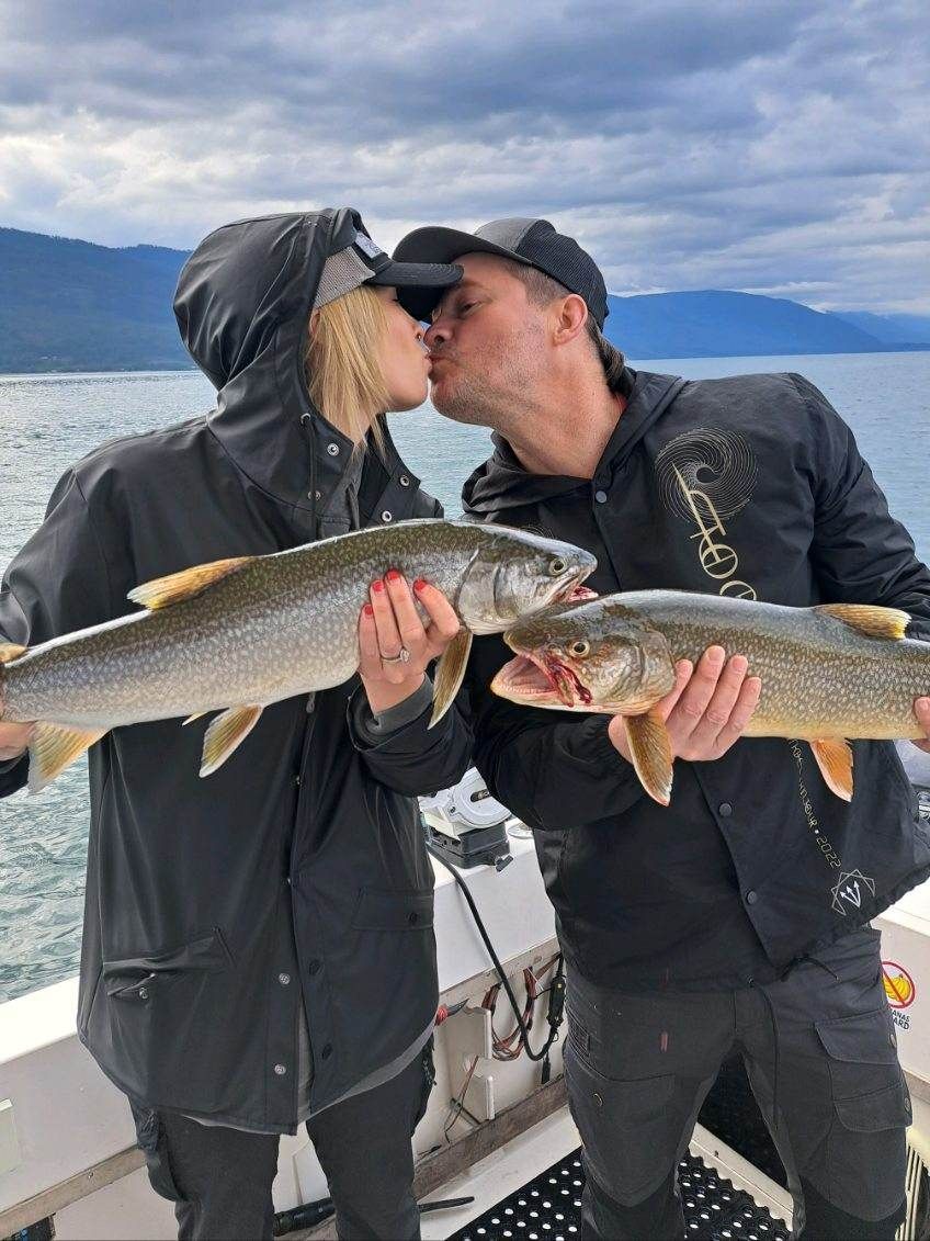 A man and a woman are kissing while holding fish on a boat.