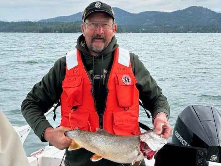 A man in an orange life vest is holding a fish on a boat