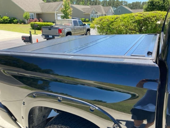 A black truck with a black bed cover is parked in front of a house.