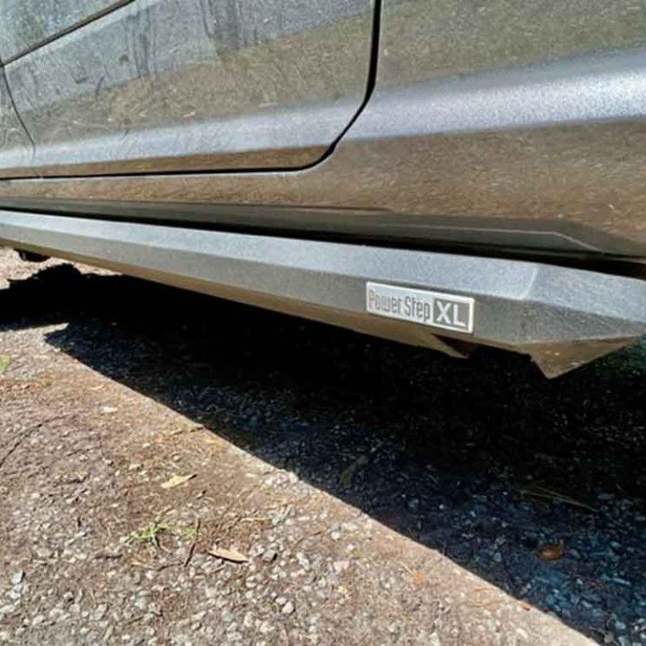 A close up of a car 's side steps on a gravel road.