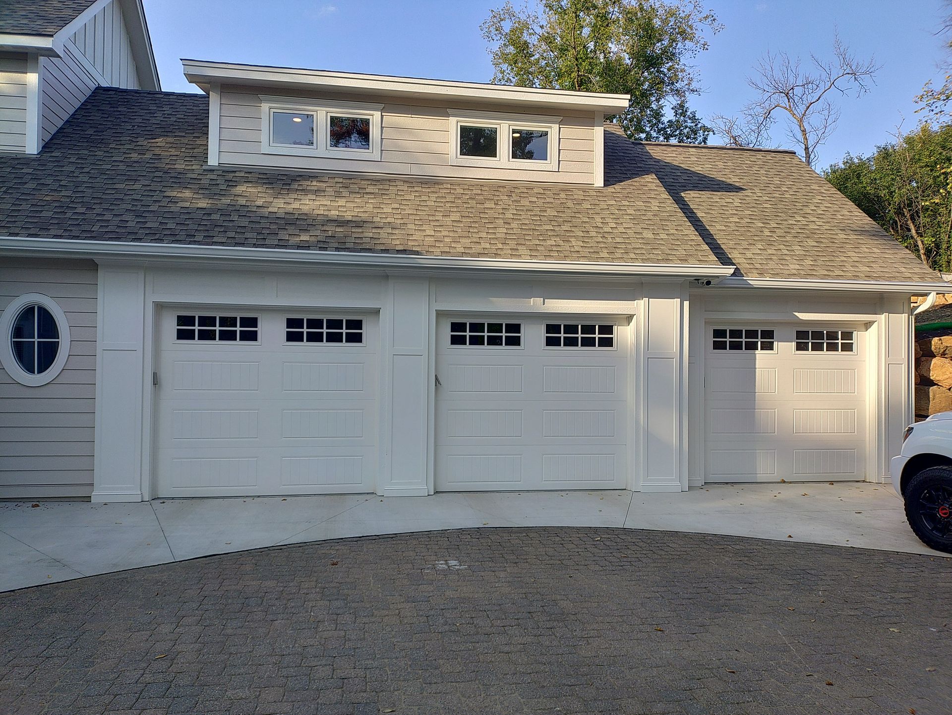 White garage doors on a building with a dormer and light-colored siding.