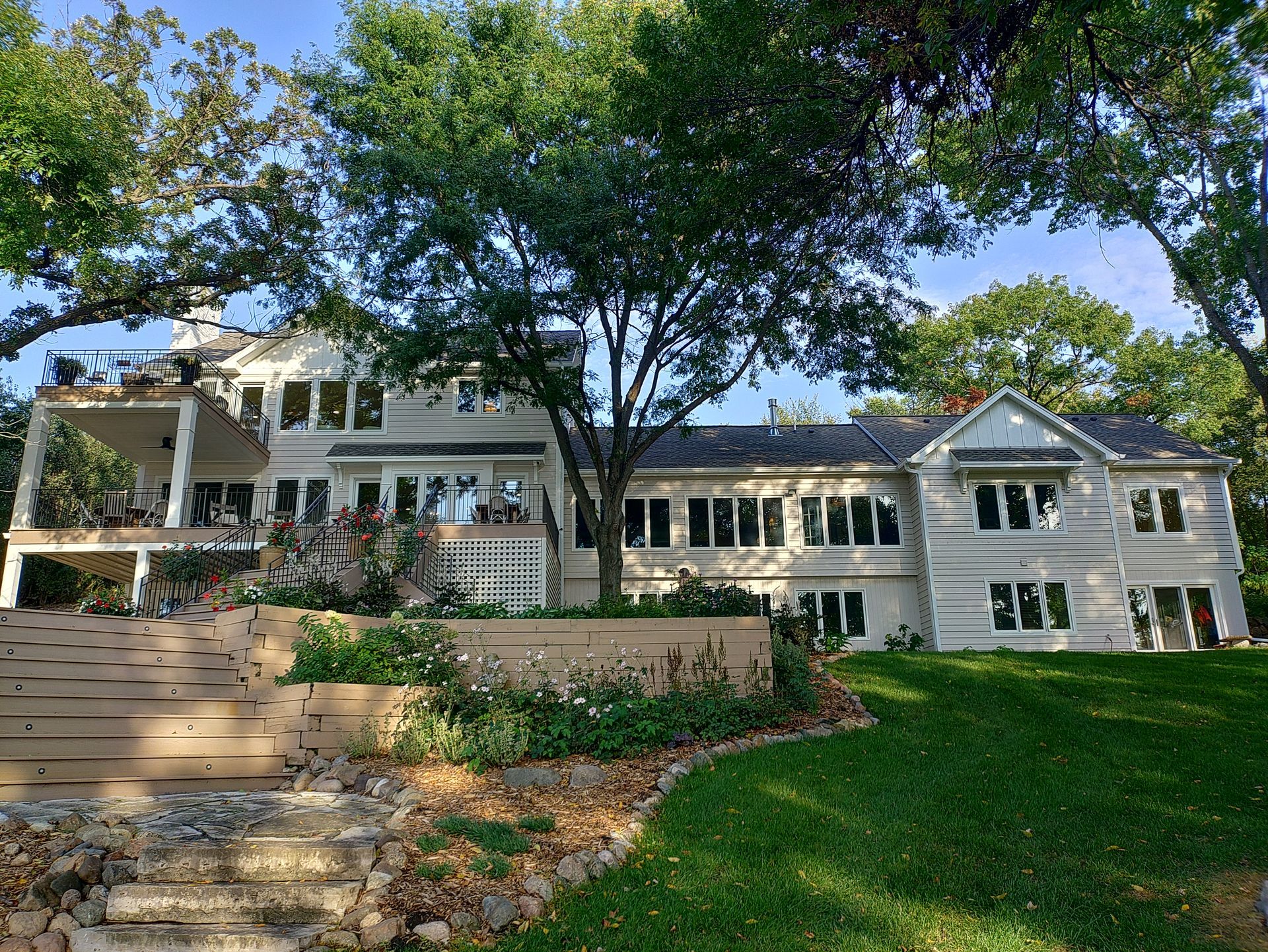 Large white house with multi-level windows, patio, and lush green lawn.