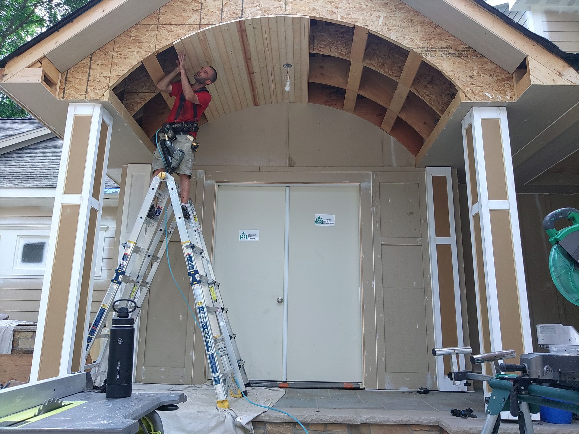 Person on ladder working on arched porch ceiling. Door visible.