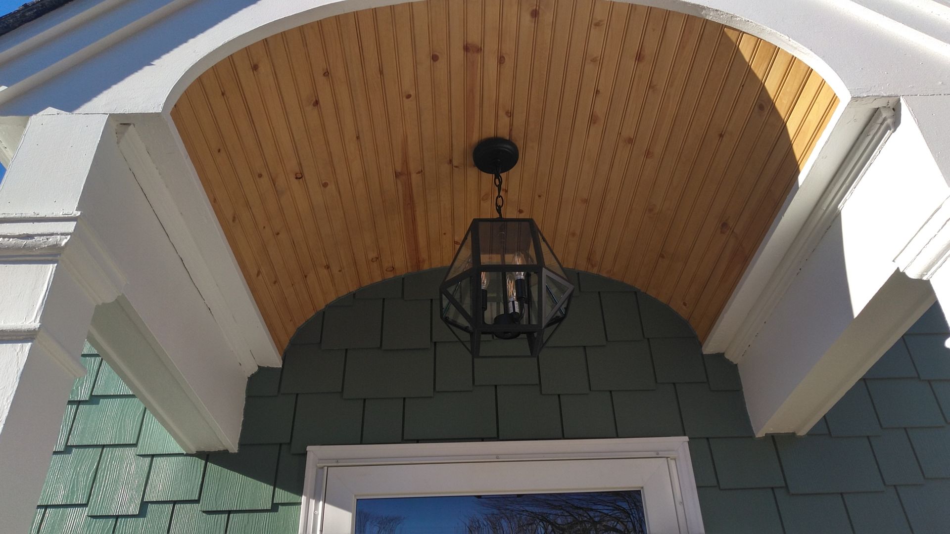 Exterior entryway with arched wood ceiling, white trim, green shingle siding, and black lantern.