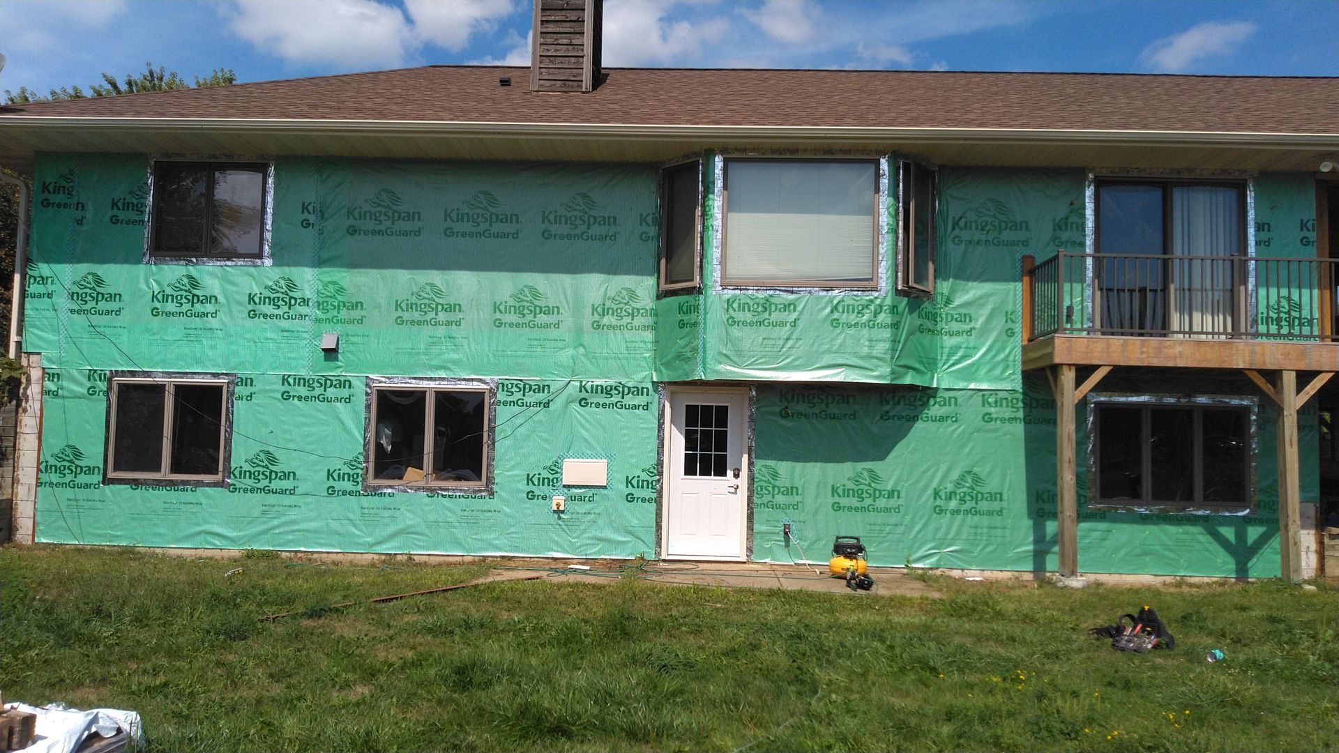 House exterior with green wrap, windows, door, and deck under construction against a blue sky.
