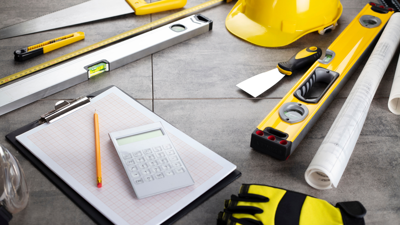 Construction tools and blueprints on tiled surface, including a saw, level, hard hat, and clipboard.