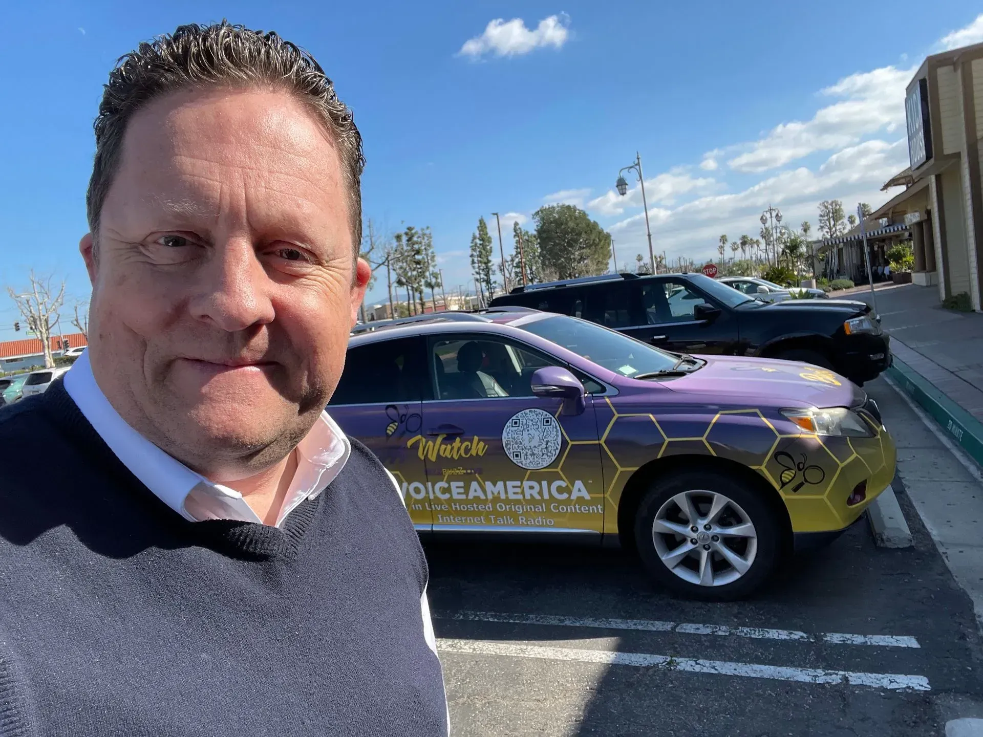 a man is standing in front of a purple car that says voice america