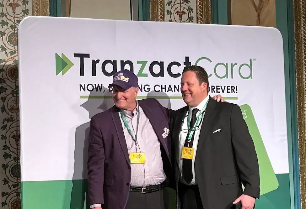 two men standing in front of a sign that says tranzact card