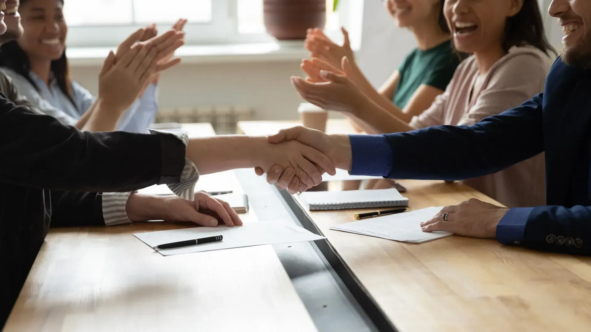 a group of people are sitting around a table shaking hands