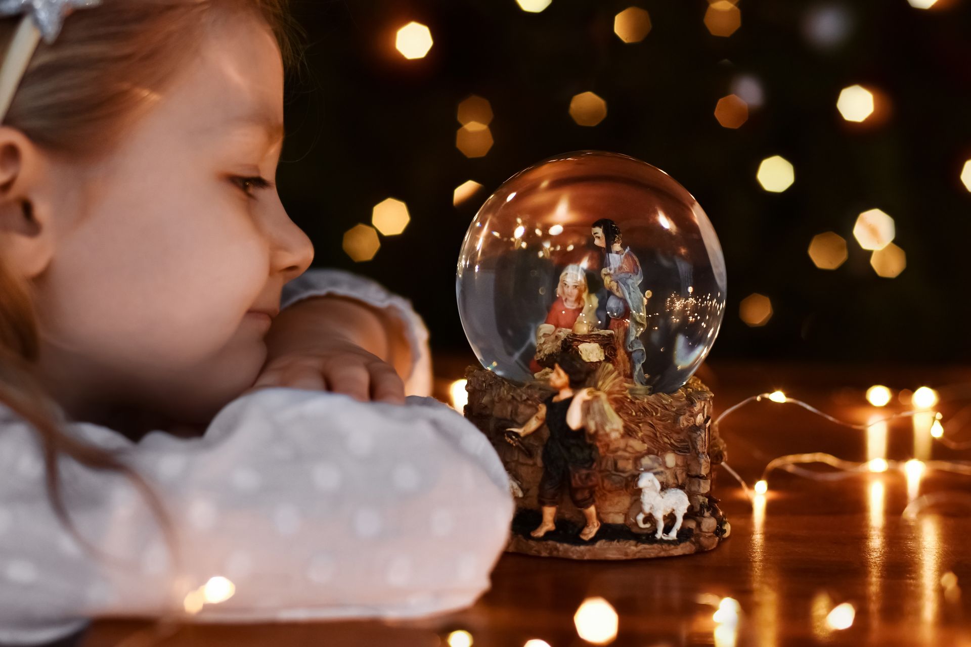 A little girl is looking at a snow globe with a nativity scene in it.