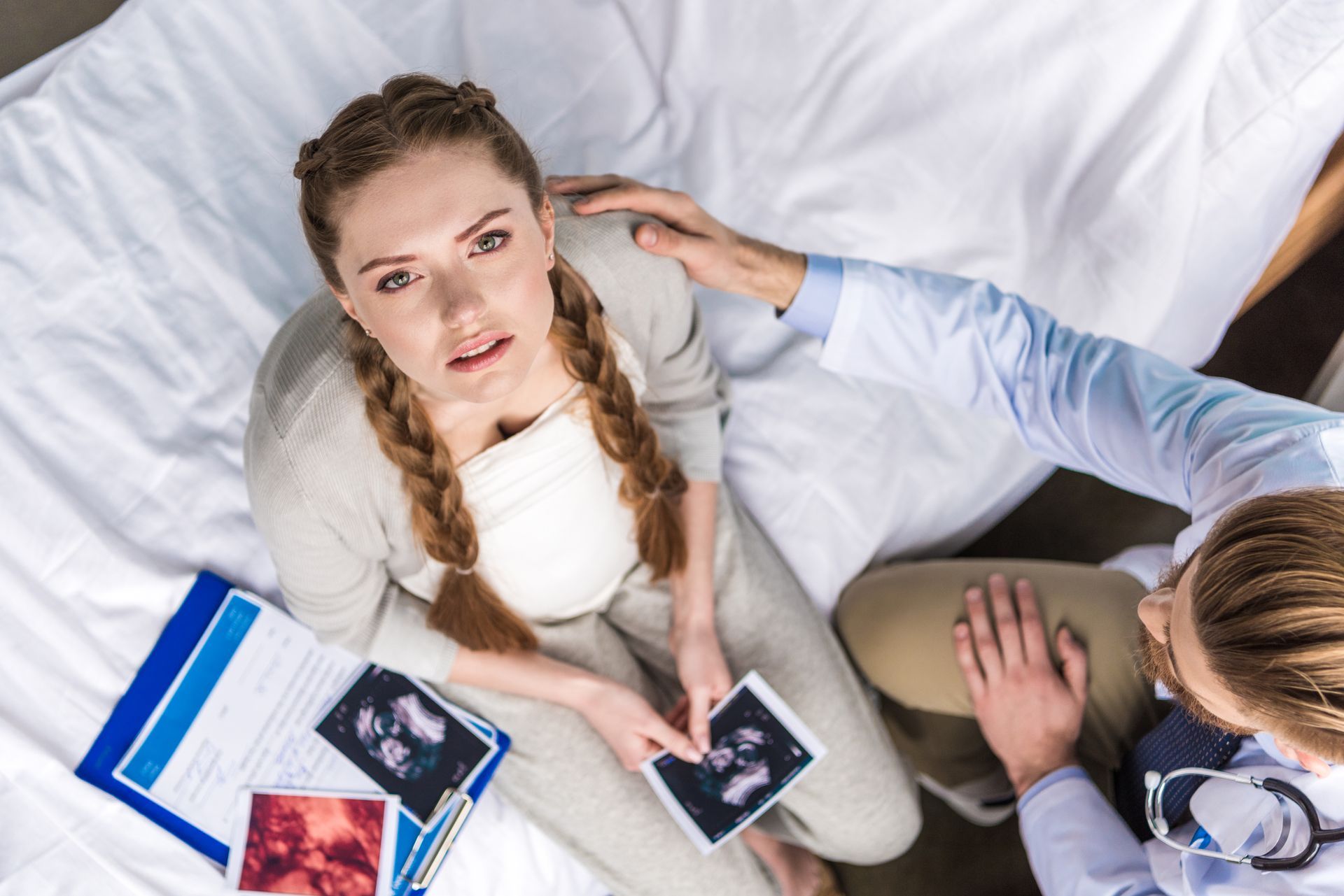 A pregnant woman is sitting on a bed talking to a doctor.