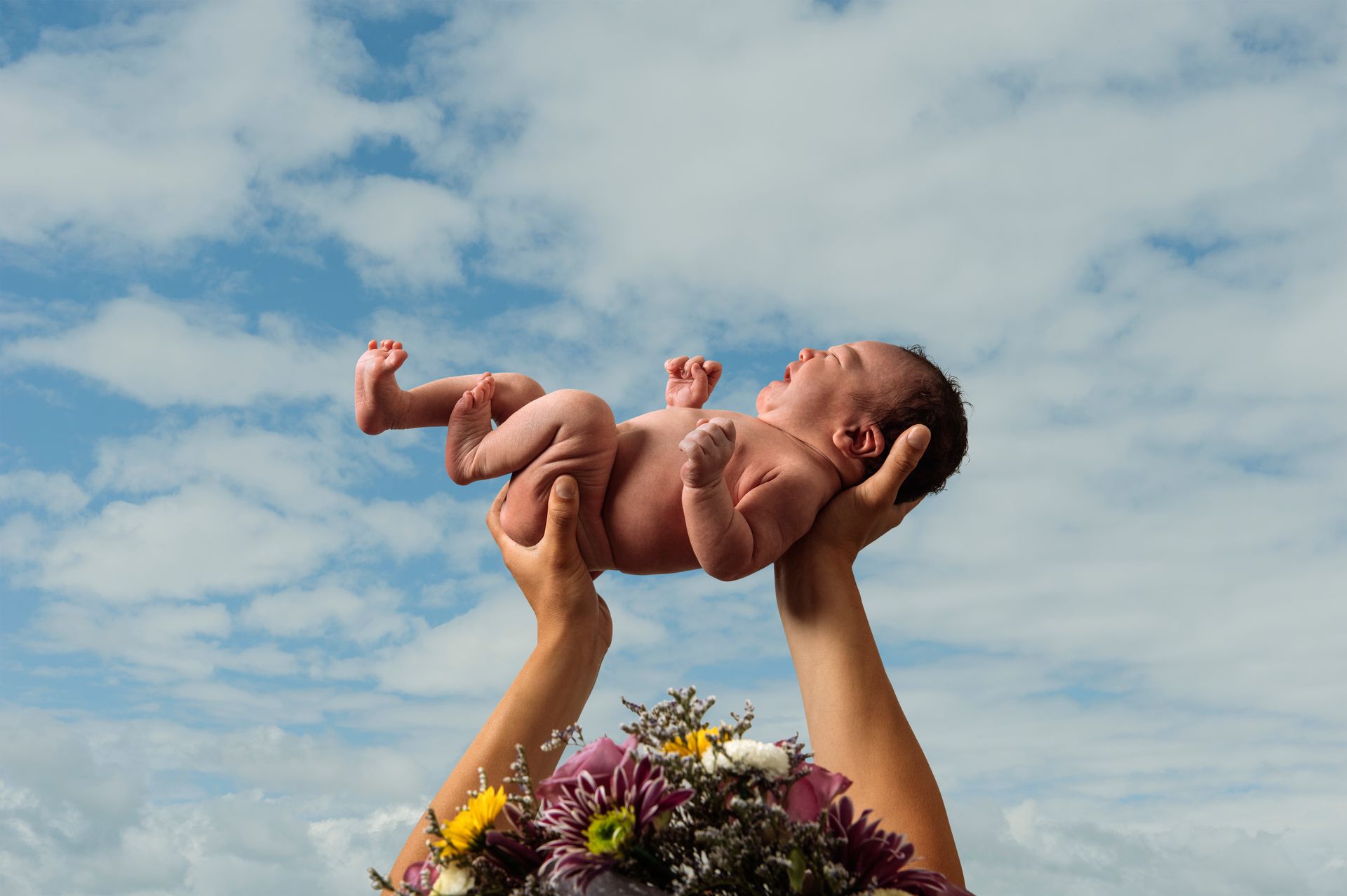 A person is holding a newborn baby in the air.