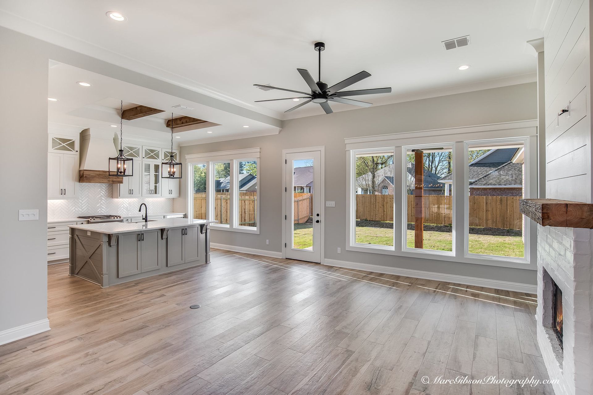 Spacious, open-concept living area with kitchen, windows, fireplace, and light wood floors.