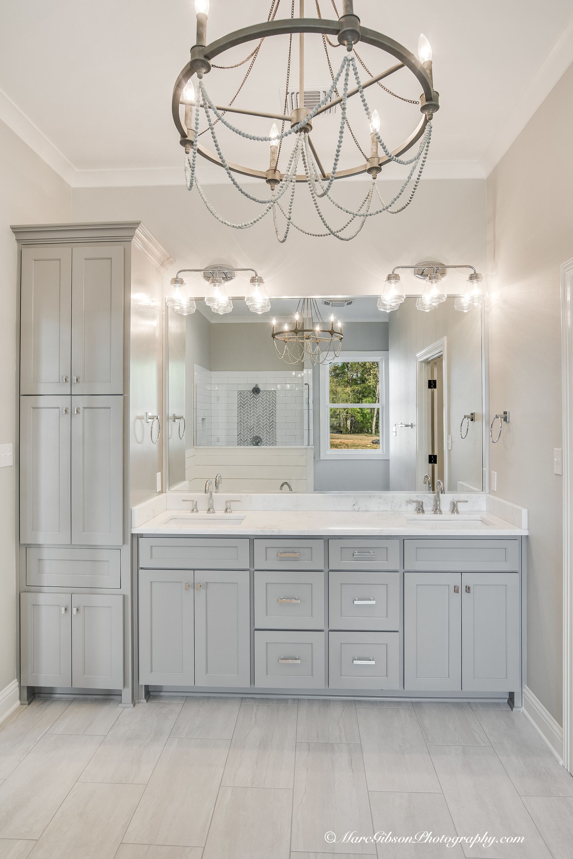 Gray bathroom with double sink vanity, storage cabinet, large mirror, and chandelier.