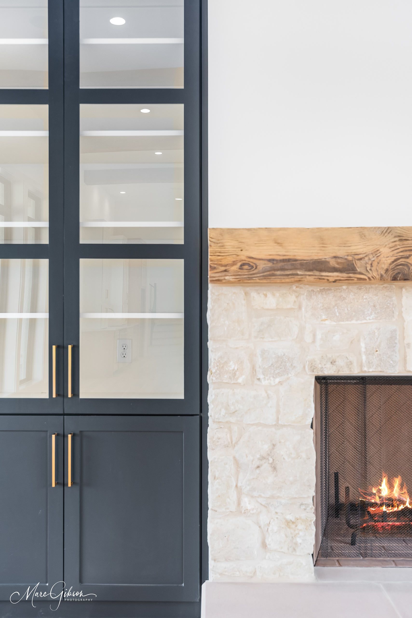 Dark blue cabinet with glass doors next to a stone fireplace with a burning fire.
