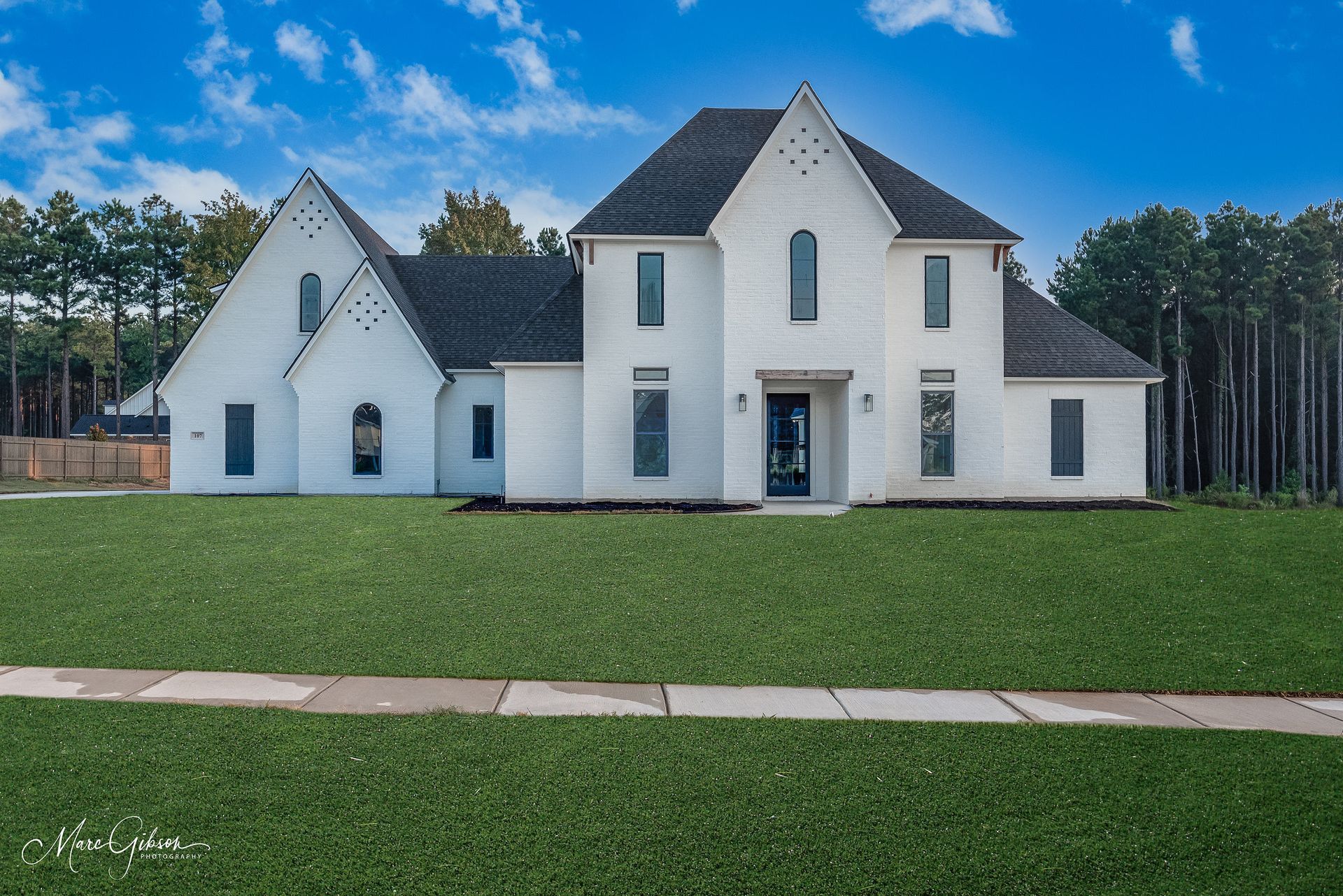 White brick house with dark roof, green lawn, blue sky.