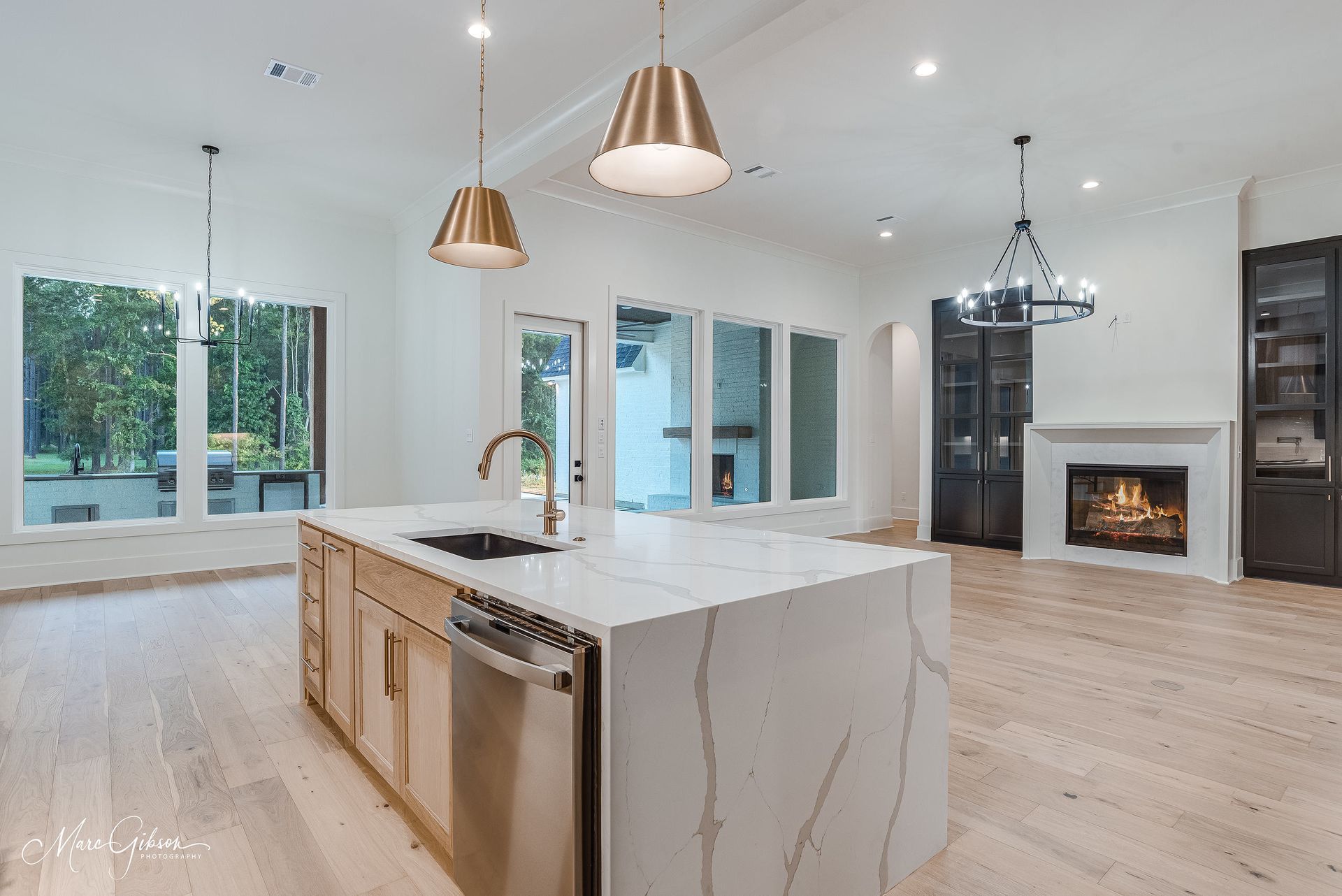 Spacious, modern kitchen with island, white countertops, wood cabinets, and fireplace.