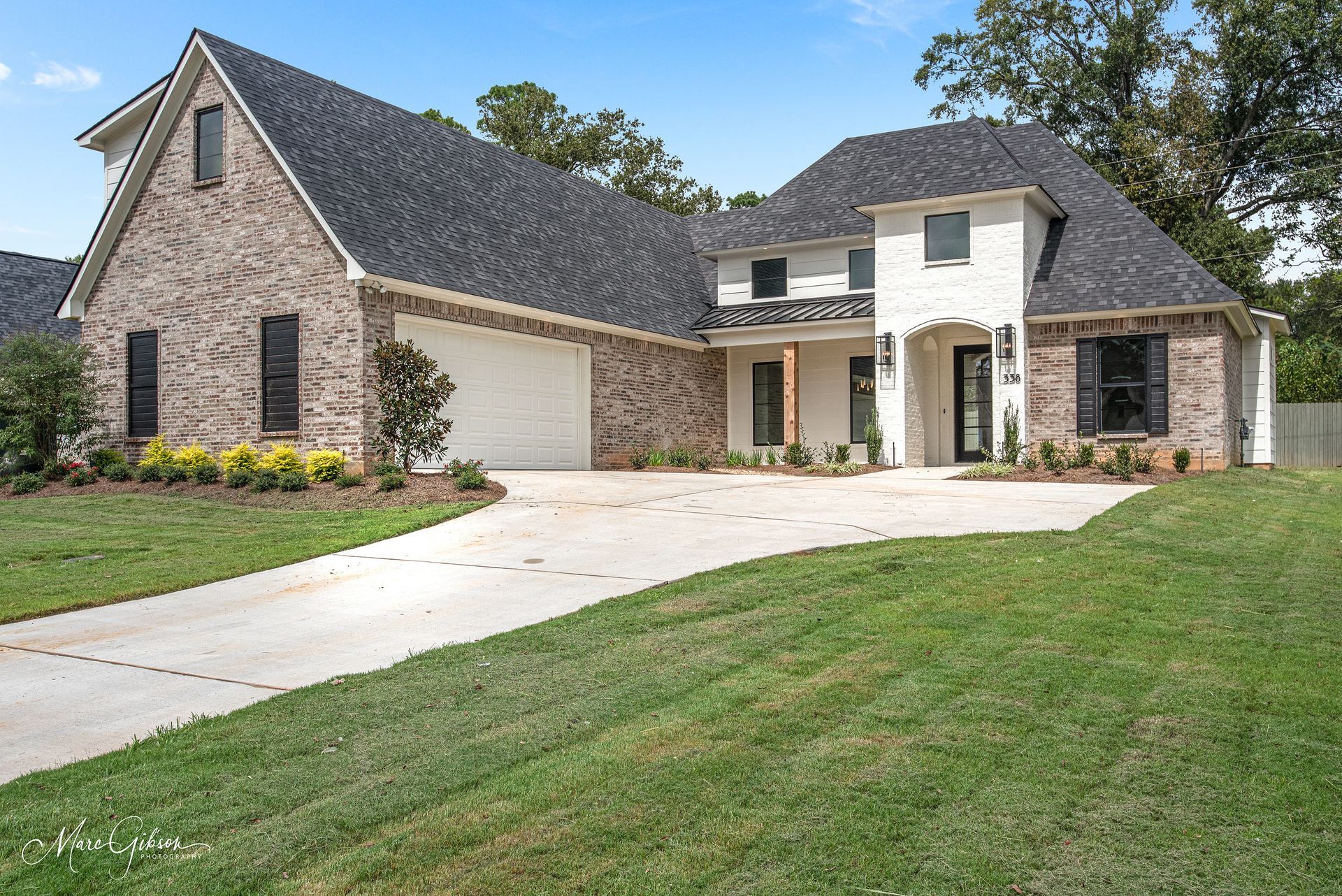 Two-story brick and white house with a long driveway, green lawn, and a blue sky.