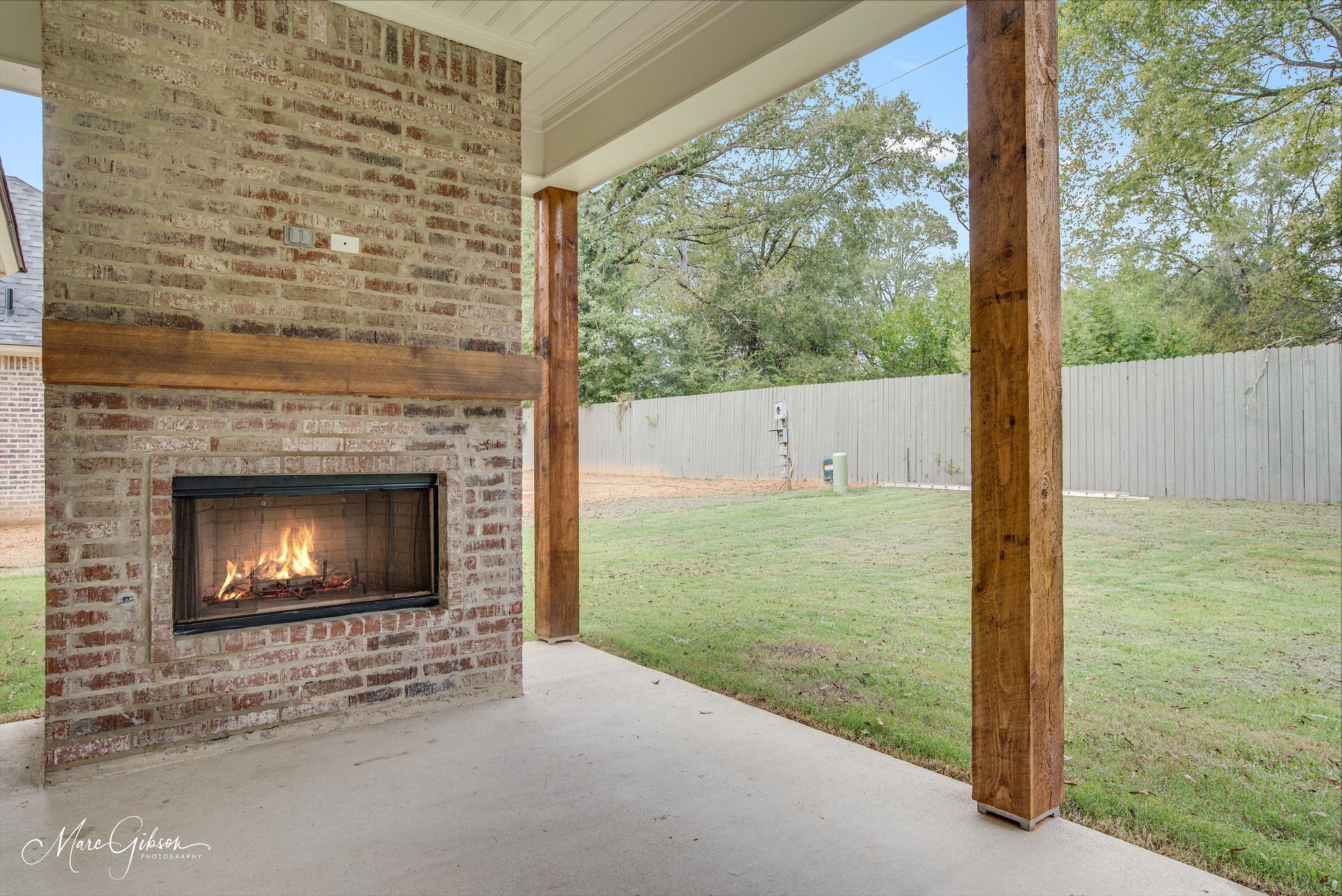 Outdoor patio with brick fireplace, wooden beams, and grassy backyard.