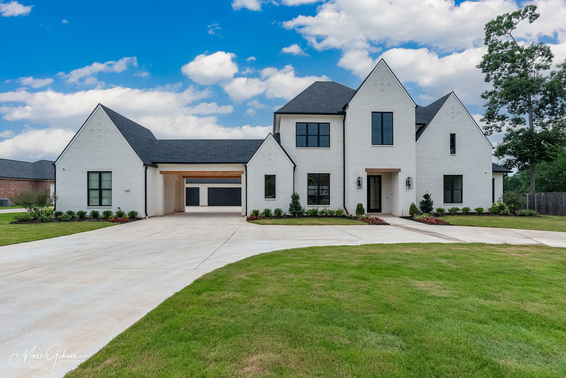 White brick house with black accents, driveway, and green lawn under a blue sky.