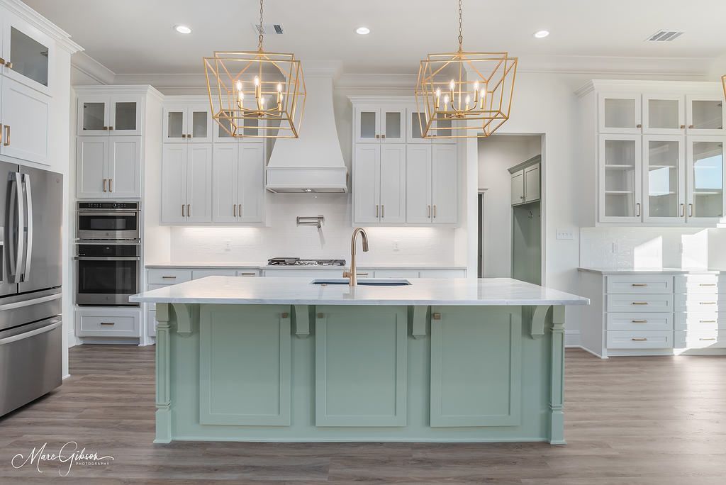 Modern kitchen with white cabinets, sage island, gold light fixtures, and stainless steel appliances.