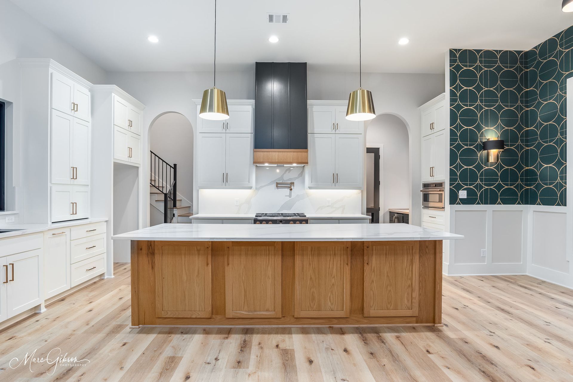 Modern kitchen with white cabinets, wood island, gold pendant lights, and geometric wallpaper accent wall.