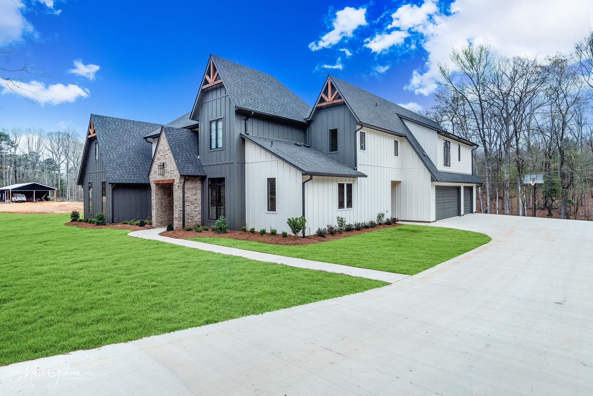Modern farmhouse with gray and white siding, brick accents, and a green lawn.