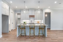 Modern kitchen with island, bar stools, and overhead lights. Gold and white color scheme.