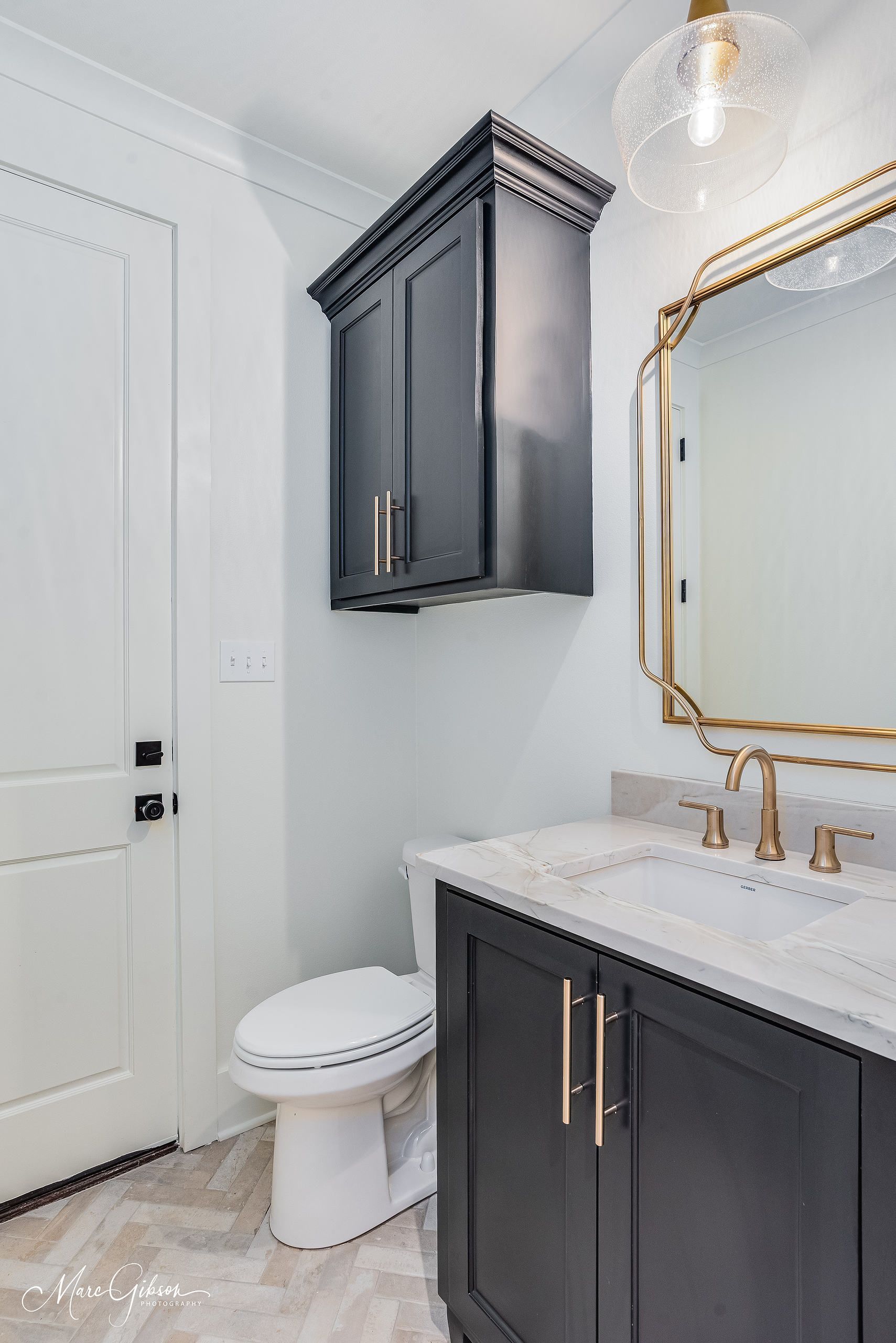 Bathroom with black vanity, toilet, and wall cabinet. Gold mirror and fixtures. White walls.