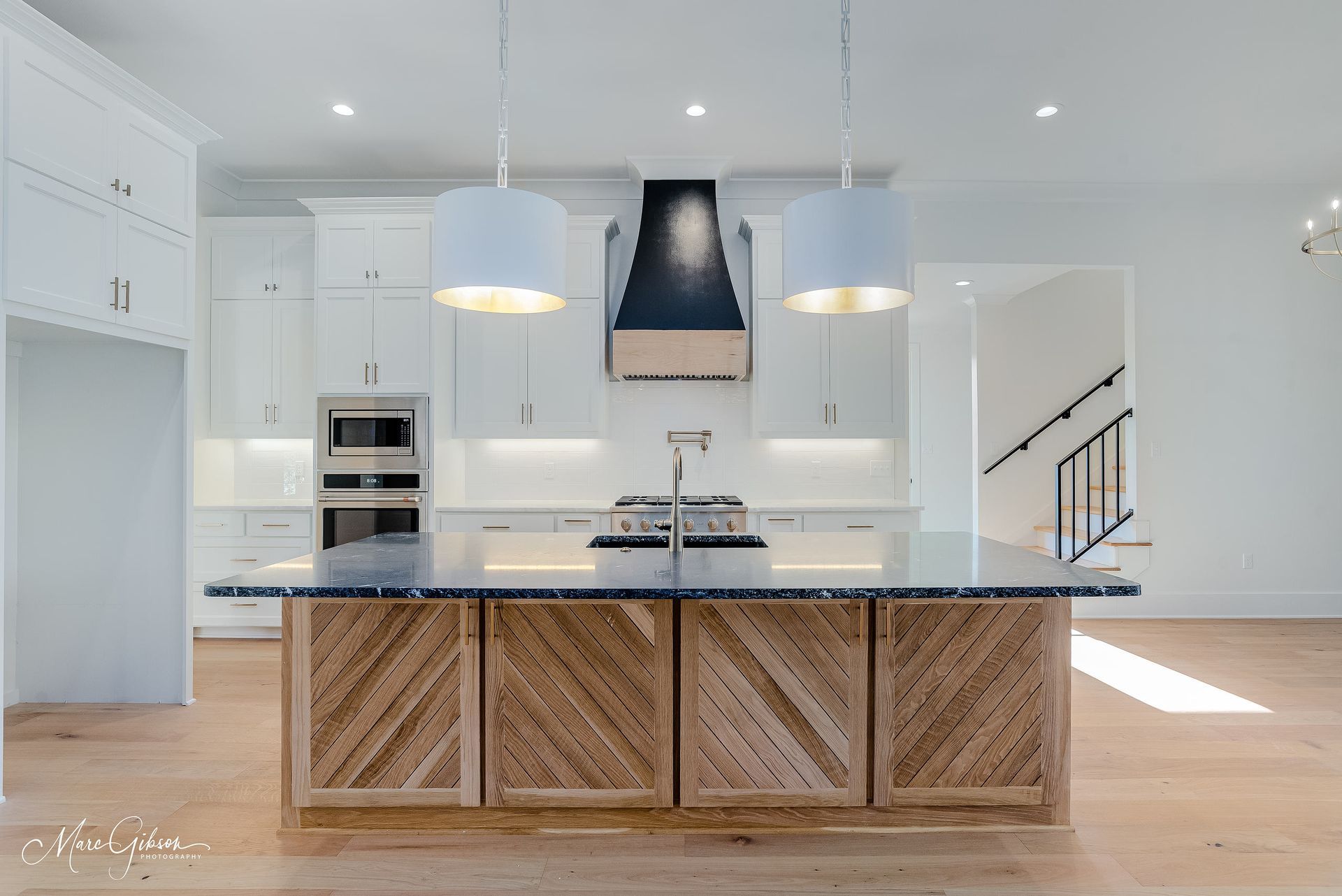 Modern white kitchen with wood island, black range hood, and pendant lights.