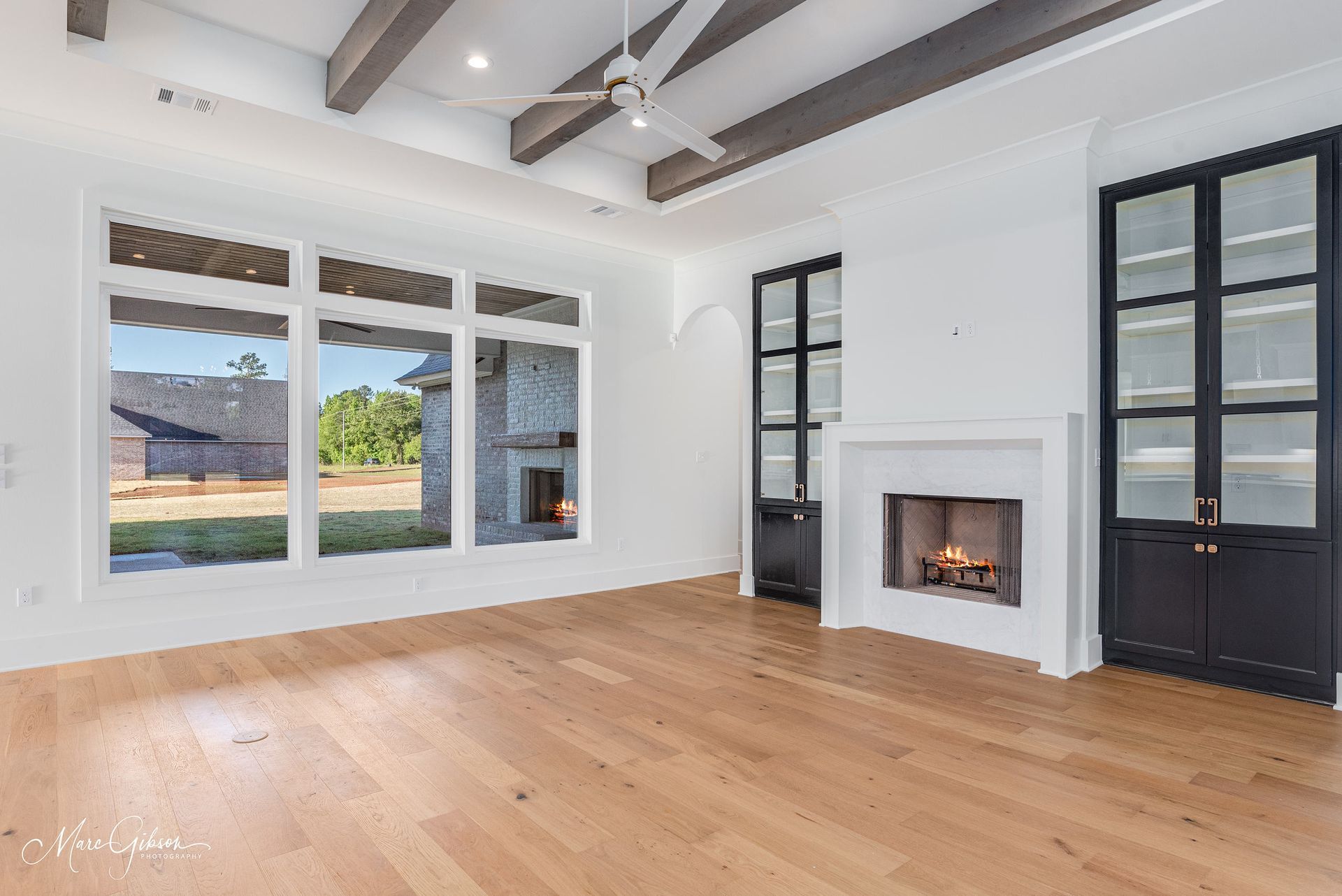 Bright living room with large windows, fireplace, wood floor, and exposed ceiling beams.