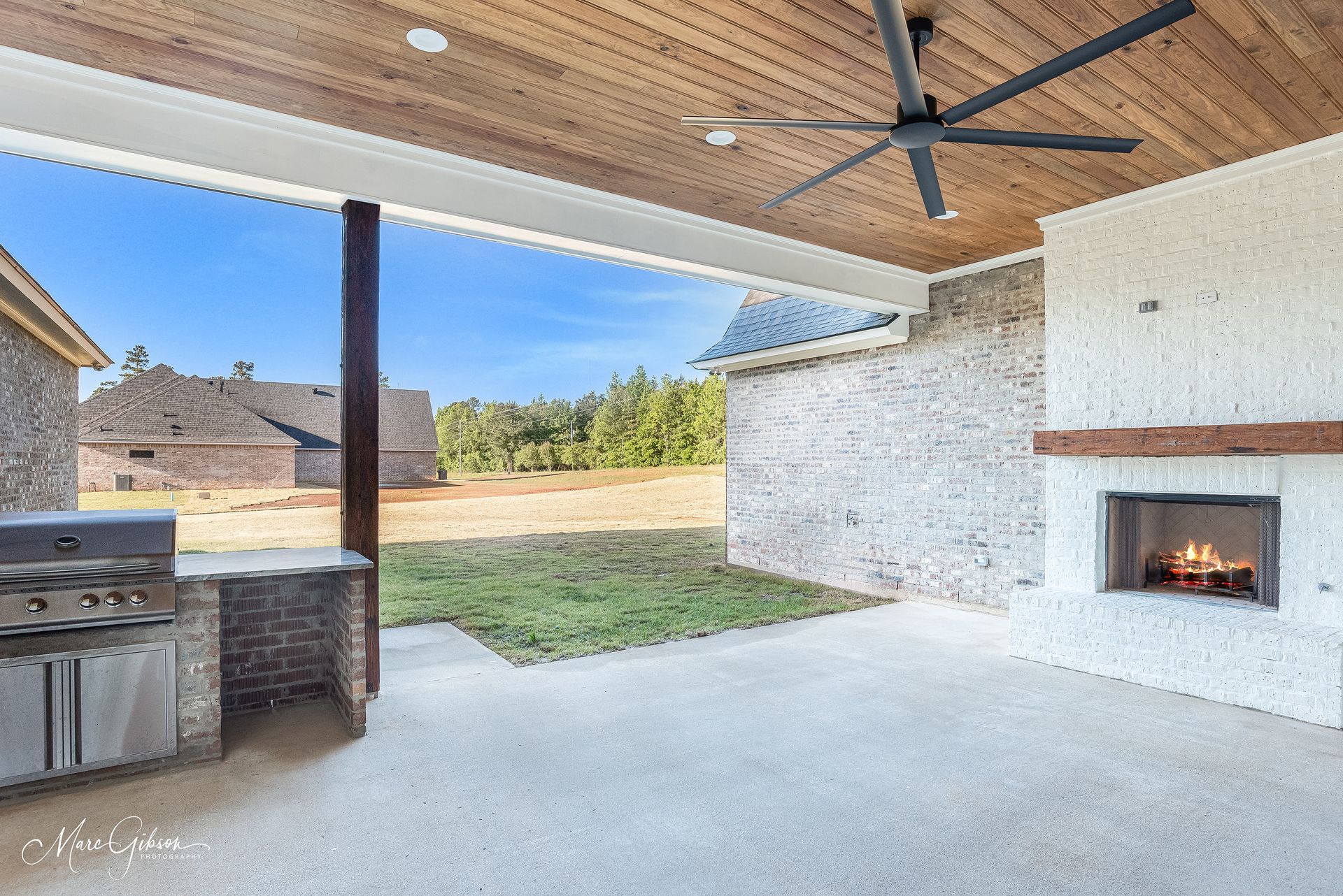 Outdoor patio with grill, fireplace, and wood ceiling. Blue sky and grassy yard visible.