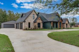 A large brick home with a green door, attached garage, and circular driveway on a grassy lawn.