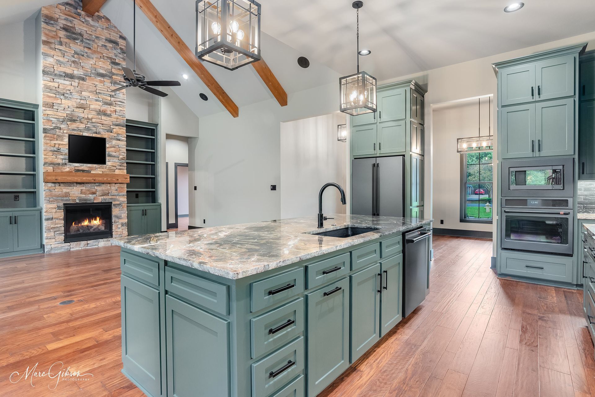 Spacious kitchen with teal cabinets, a large island, fireplace, and hardwood floors.