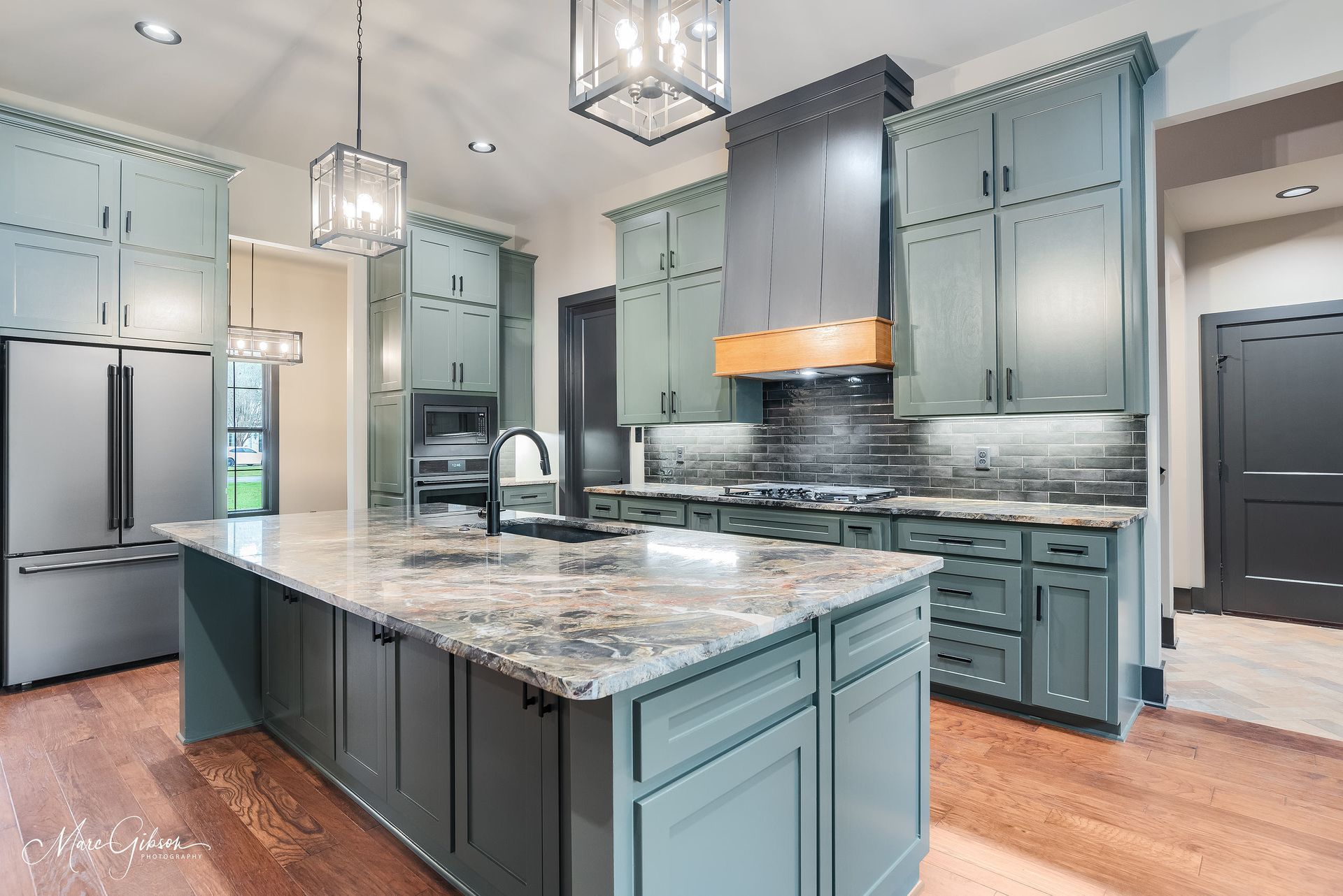Spacious kitchen with blue-green cabinets, large island, stainless steel appliances, and wood floors.
