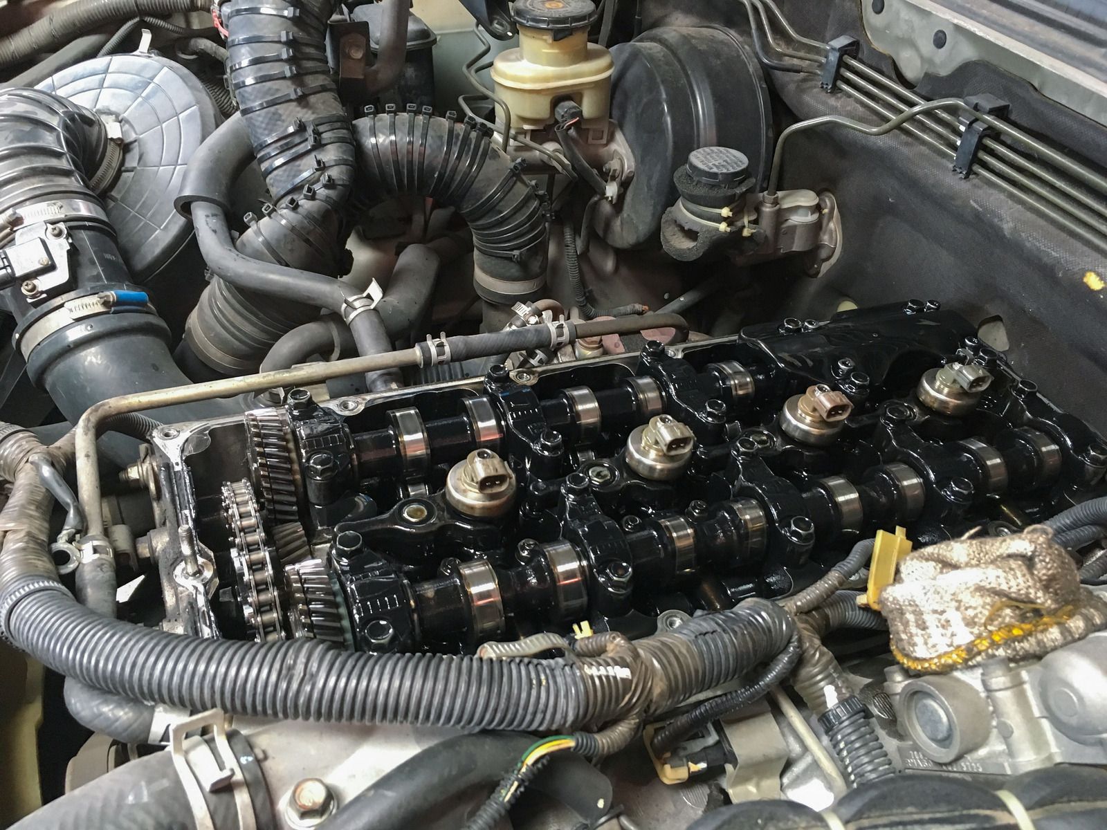 Open car engine with exposed valve train, coated in black oil, under the hood of a vehicle.