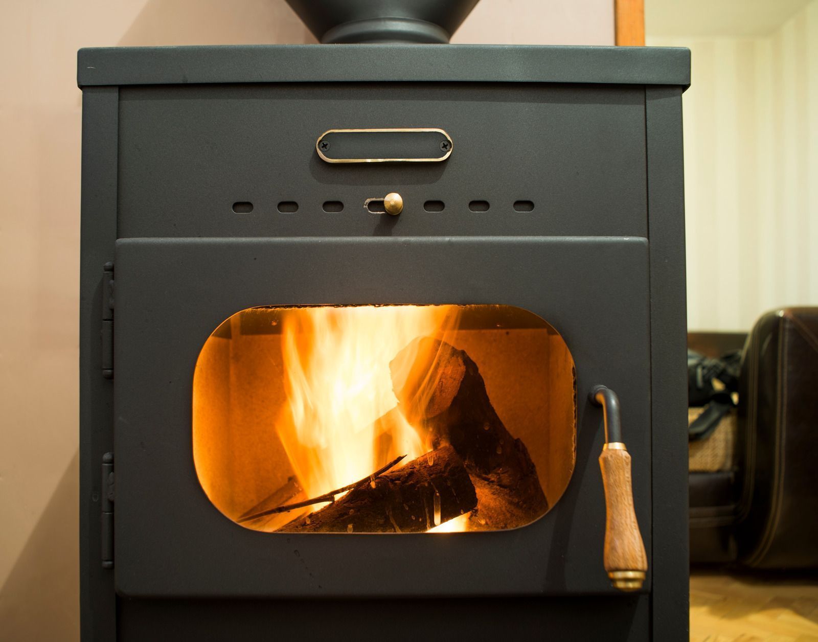 Dark gray wood-burning stove with flames visible through the glass door; wooden handle.