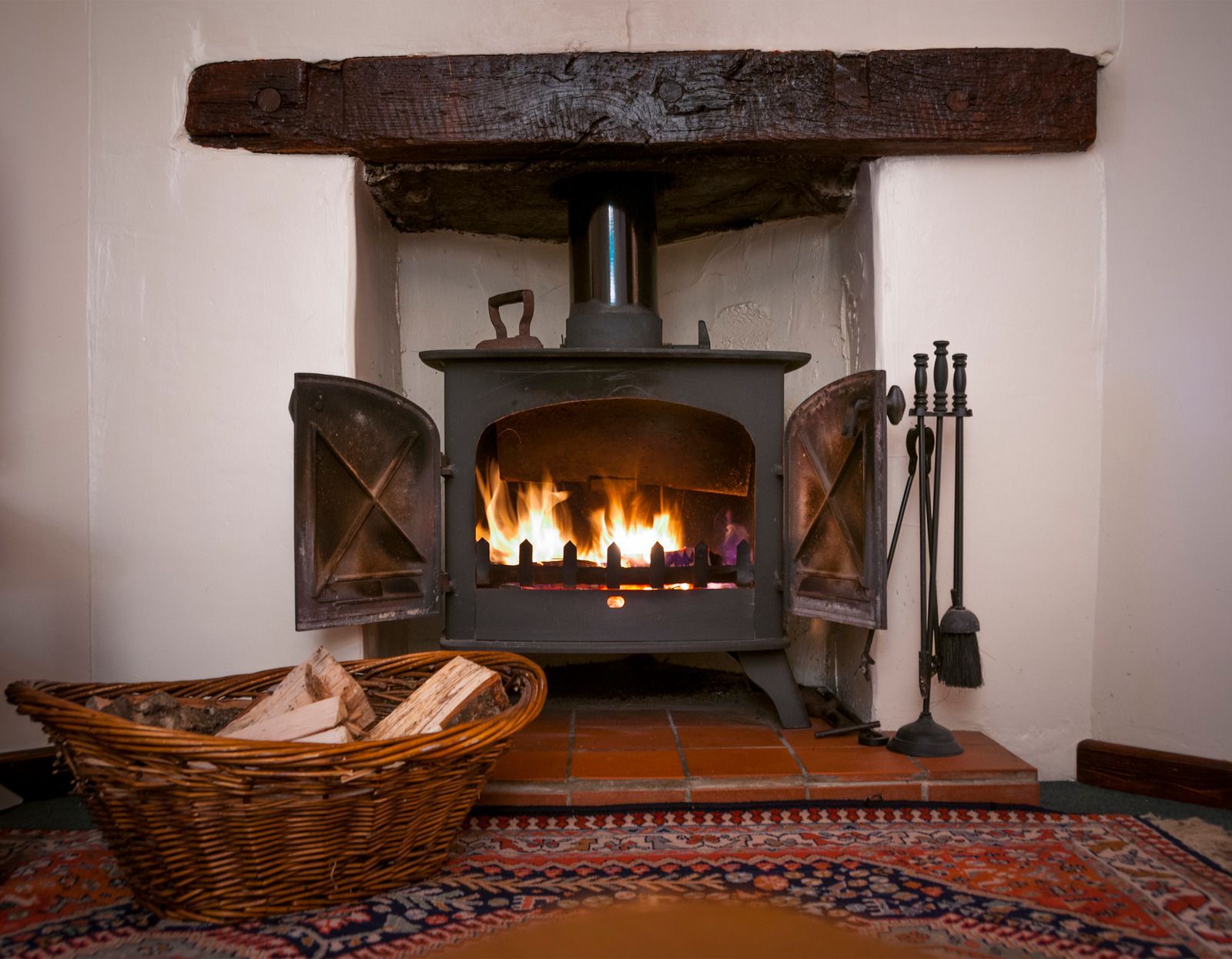 Wood-burning stove with flames in a brick fireplace, basket of logs nearby.