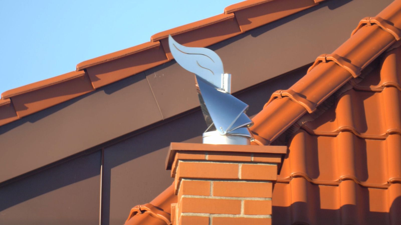 A brick chimney on top of a red tiled roof.