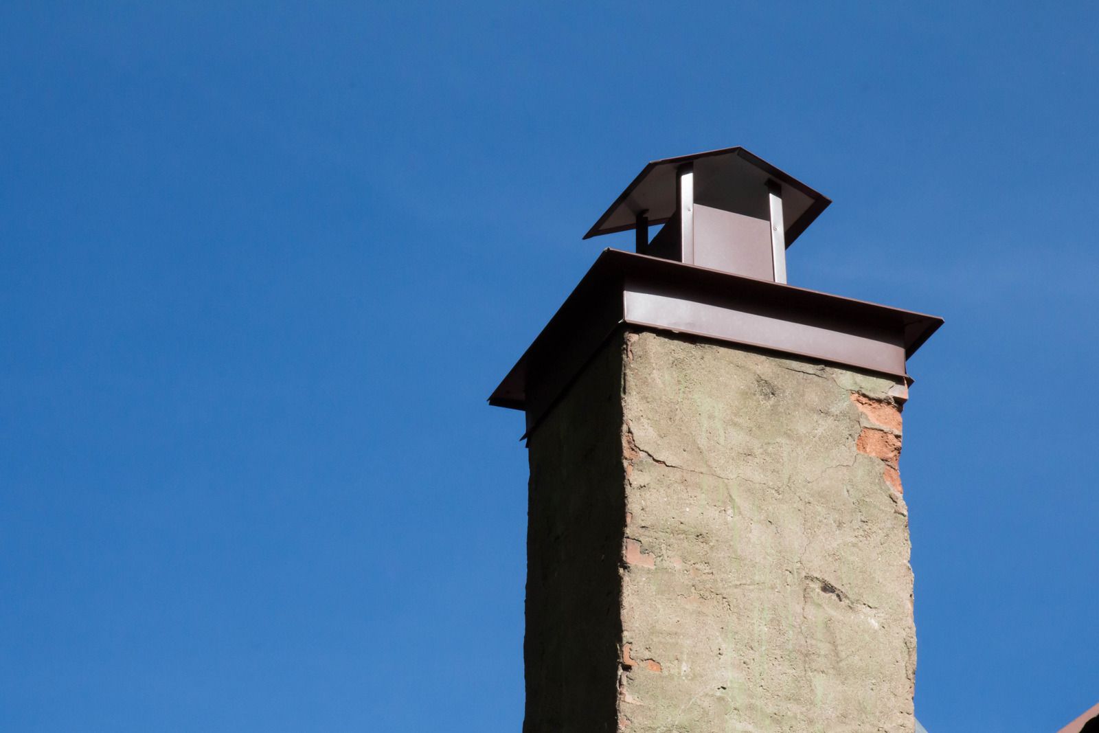 Stone chimney with a small black vent cap against a clear blue sky