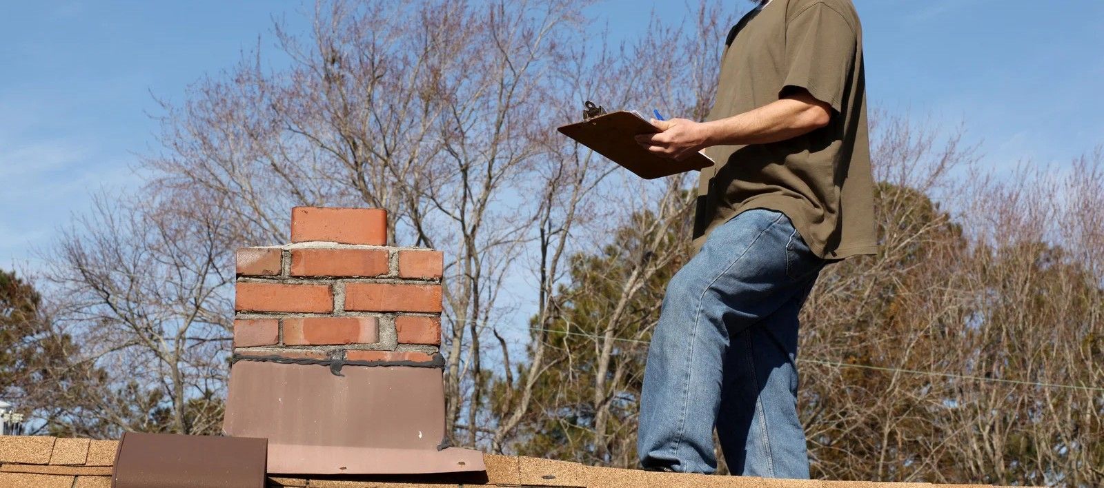 A man is standing on a roof looking at a clipboard.