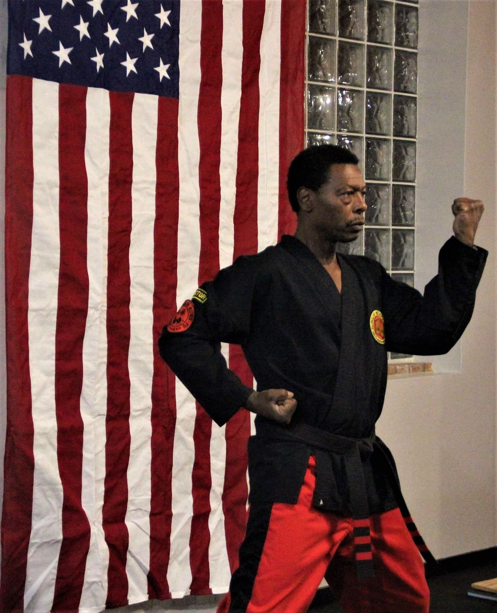 A man in a karate uniform stands in front of an american flag