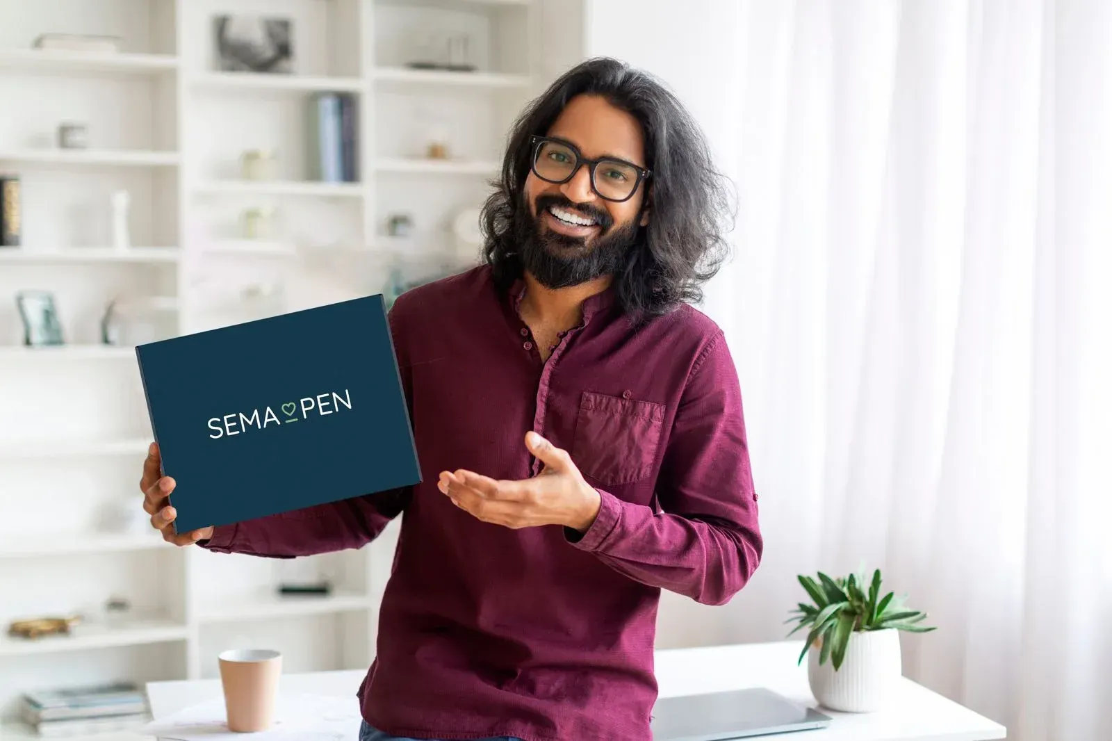 An asian man is holding a SemaPen box. He has a big open smile on his face.