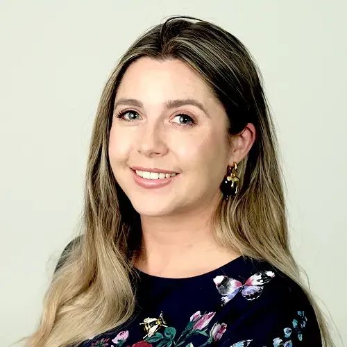 A woman wearing a floral shirt and earrings is smiling for the camera.