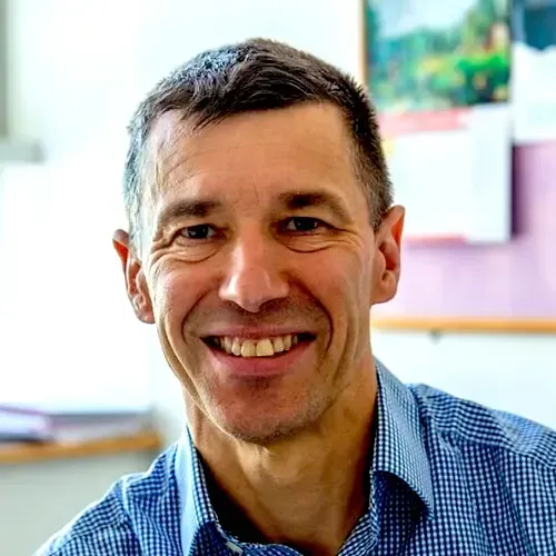 A man in a blue plaid shirt is smiling for the camera.